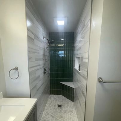 A contemporary shower space with green tiled walls, a practical bench, and elegant fixtures.