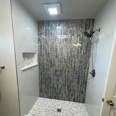 A modern shower space featuring a rainfall showerhead, a tiled wall with vertical gray tiles, and a mosaic tile floor.