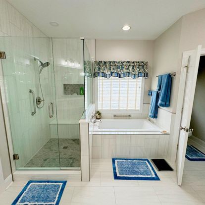 A bright bathroom showcasing a glass shower enclosure, a bathtub, and blue accent towels and rugs.