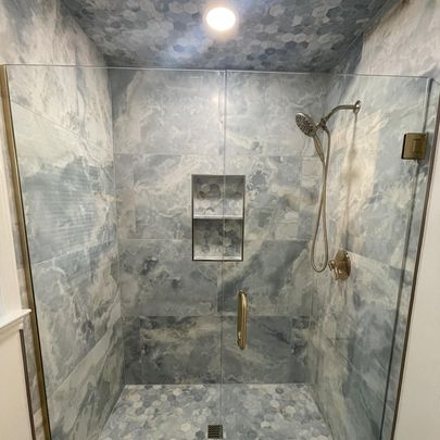 A luxurious shower area with marble tiles, a built-in shelf, and a showerhead.