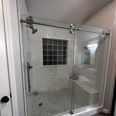 A modern shower with clear glass doors, surrounded by white tiles and a window for natural light.