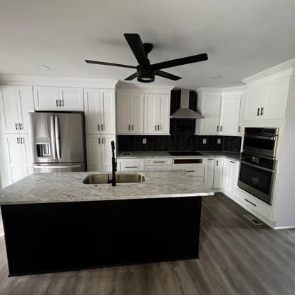 A stylish kitchen with white cabinetry, a dark patterned backsplash, an island with a sink, and modern appliances.