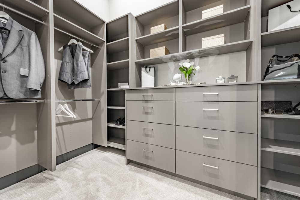 A well-organized closet featuring grey shelves, clothing, and storage options like drawers and open compartments.